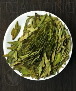 The roasted leaves of the green tea Longjing Traditional Supreme on a small white dish