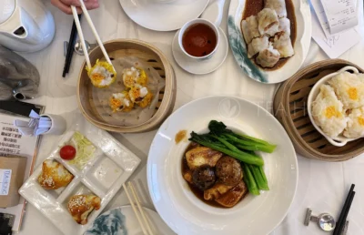 on a table covered with various dimsums and other small dishes of food, a cup filled with a dark bungundy tea liquor of Pu'er tea