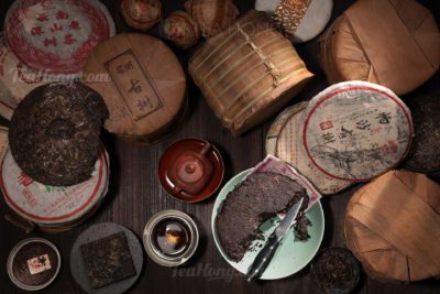 Piles of compressed tea discuses, some open and chipped for making tea, some in wrapped form, some in the original bamboo bark wraps