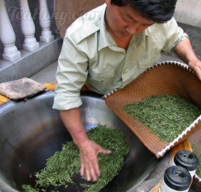 Leaves being scooped back into a bamboo sieve to cool down