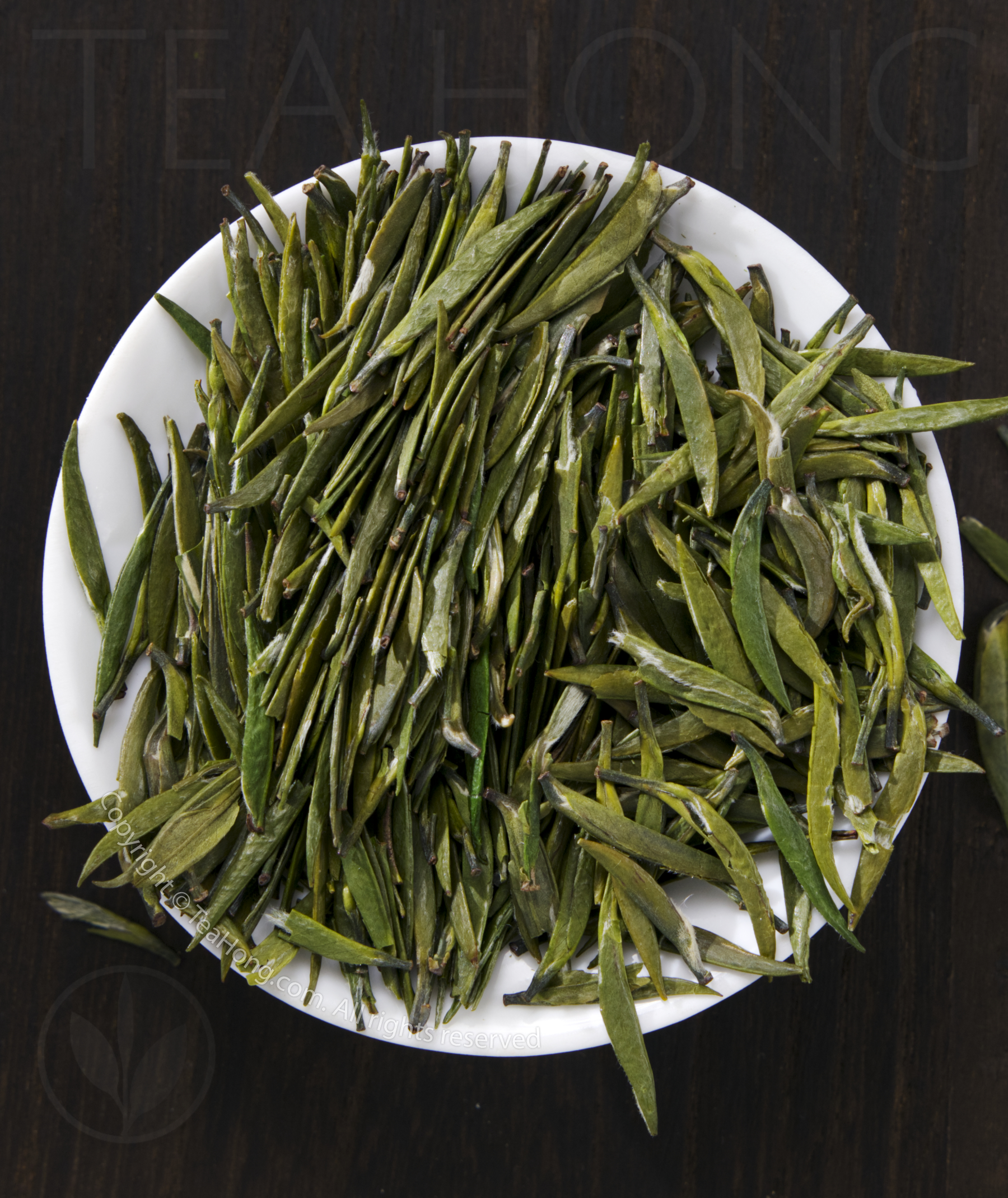 Tea Hong's Bamboo Leaf, a classic pressed wok roasted green tea the flat, bamboo leaf shape leaves of the classic green tea Bamboo Leaf, piled in a small round white dish, showing the characteristics visual quality of the tea