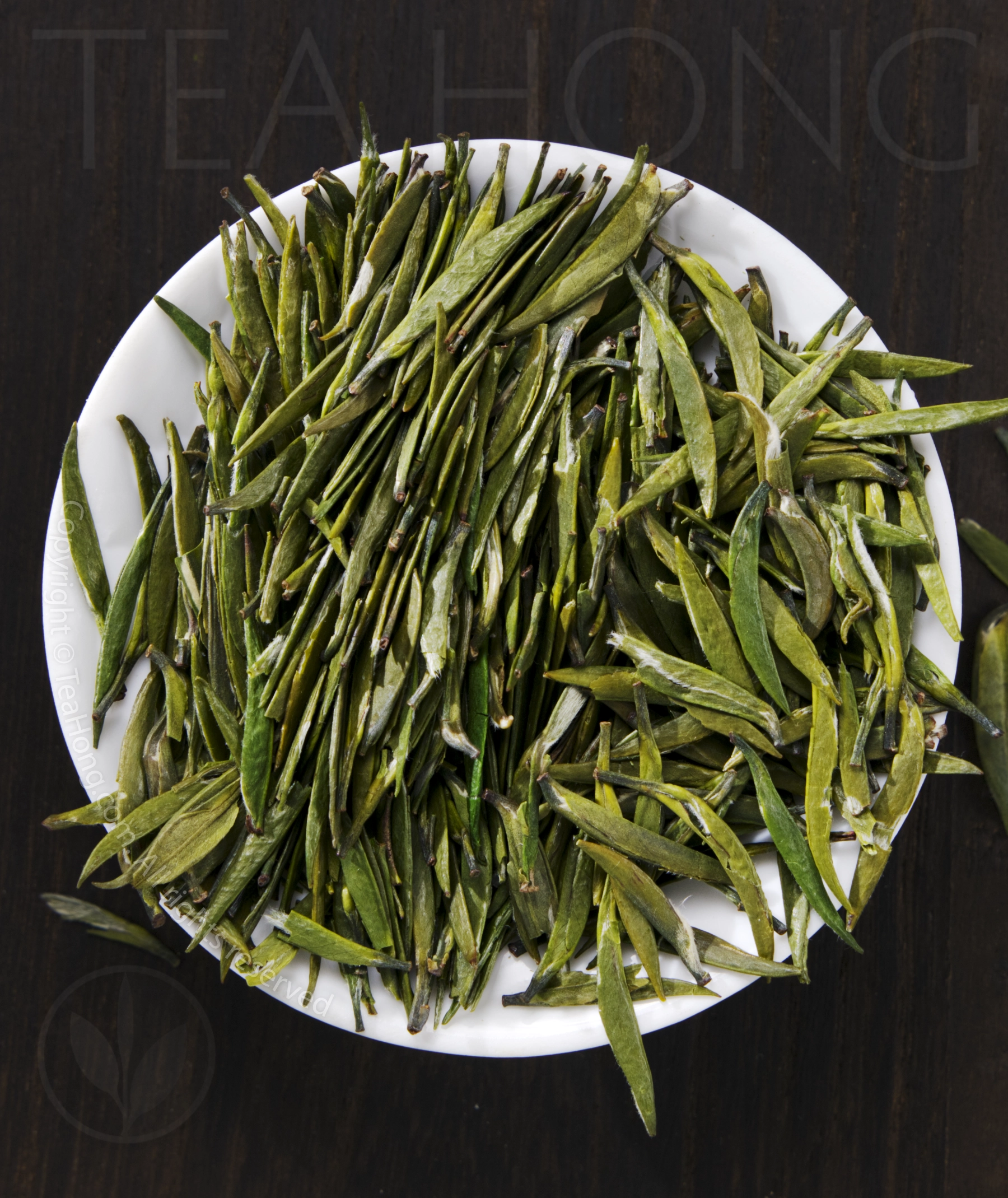Tea Hong's Bamboo Leaf, a classic pressed wok roasted green tea the flat, bamboo leaf shape leaves of the classic green tea Bamboo Leaf, piled in a small round white dish, showing the characteristics visual quality of the tea
