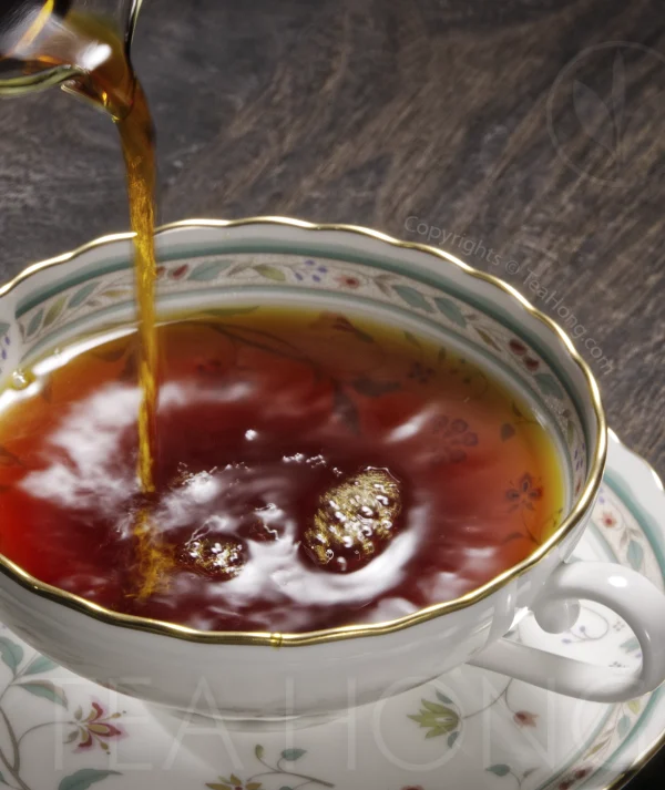 An intensely deep red, transparent tea liquor being poured into a fine porcelain Western style teacup 