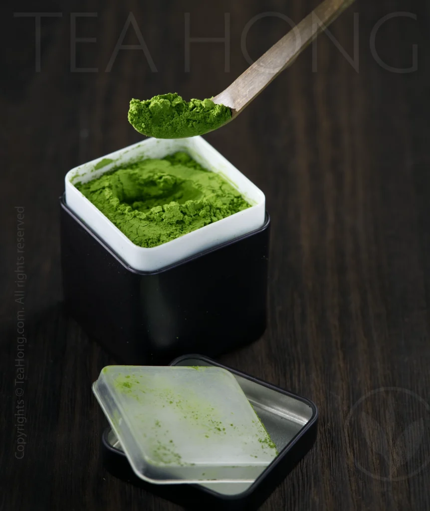 The tea tin opens showing a food grade PE inner core for holding the matcha. A bamboo matcha ladle — chasyaku — scoops out a spoonful of the tea powder