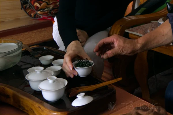 The hands of two person reaching out for a gaiwan filled with tealeaves on an infusion table with several other gaiwans and teacups