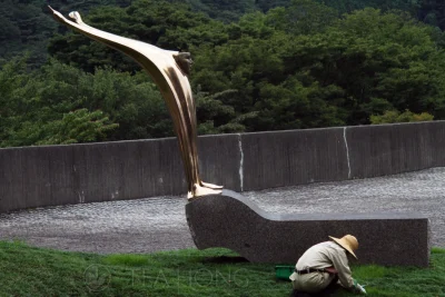 A worker attending to the lawn under and shinny bronze sculpture of a man in a shocked expression, raising two arms