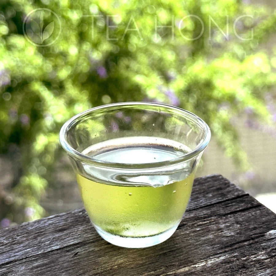 a small glass of ice cold green tea, with condensation covering the outside of the glass, and a transparent light green liquor inside
