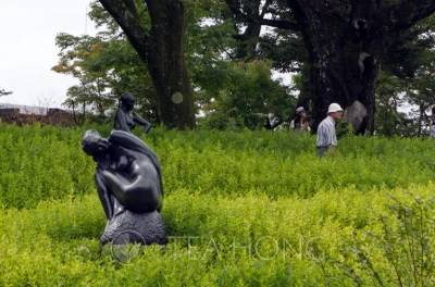 Two human size metal statues in one of the grassland areas, with two visitors walking by