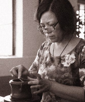 A woman artist carefully refining a curve on a teapot