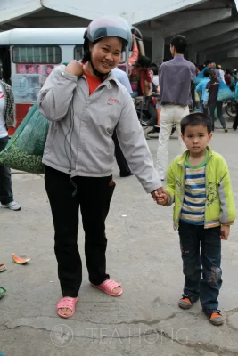 A woman with two small bags of jasmine flower buds while holding the hand of her little boy