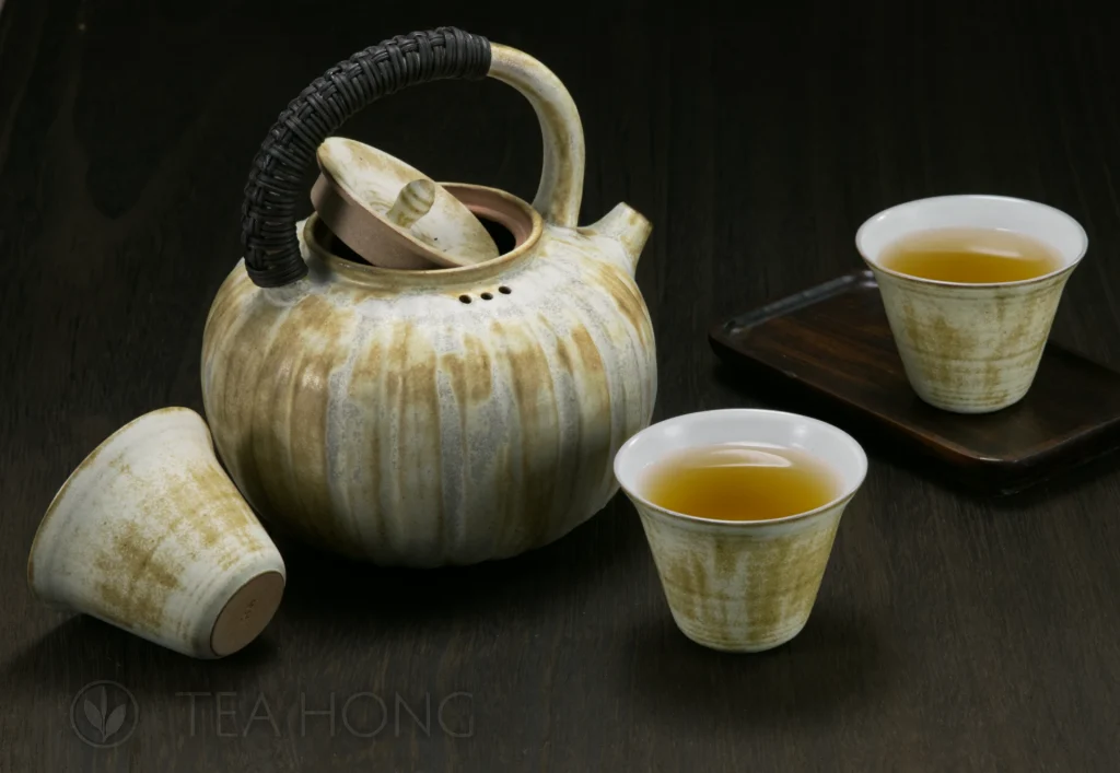 An earthenware teapot with a rustic brownish-yellow overglaze, and three matching teacups