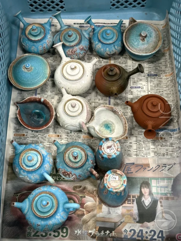 Almost 20 pieces of teapots and other teawares, in different styles and colours, a lot in bright blues. in a plastic basket lined with old newspaper