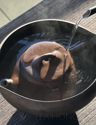 A Yixing teapot submerged in a hot water bath, with hot water pouring around it