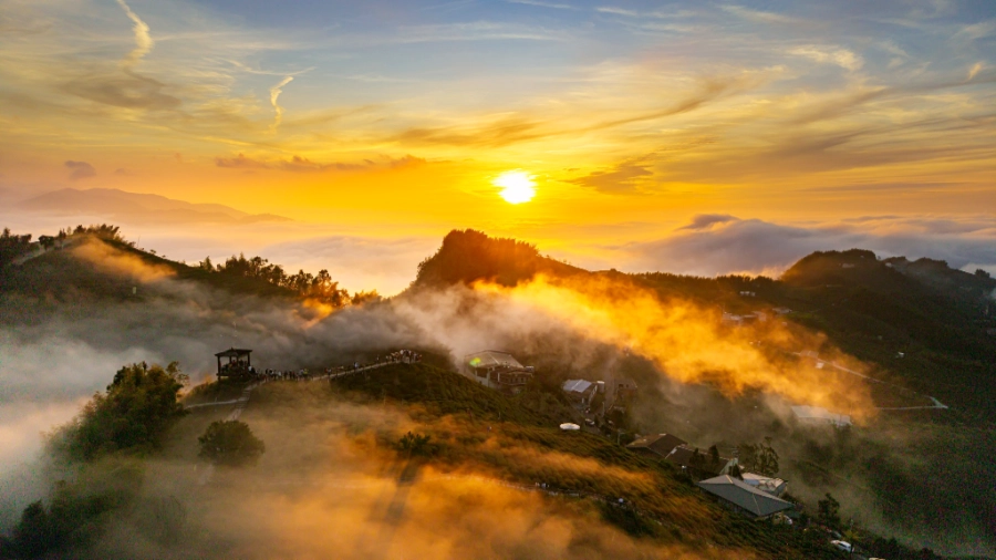 Sun set on a mountain ridge area submerged in clouds and mists, reflecting the sunlight's bright orange colours