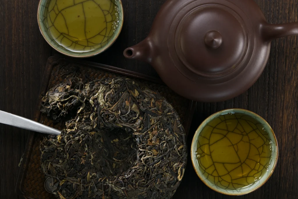 The Inner Primeval Earth cha bing chipped, posed together with a Yixing teapot and two teacups filled with tea