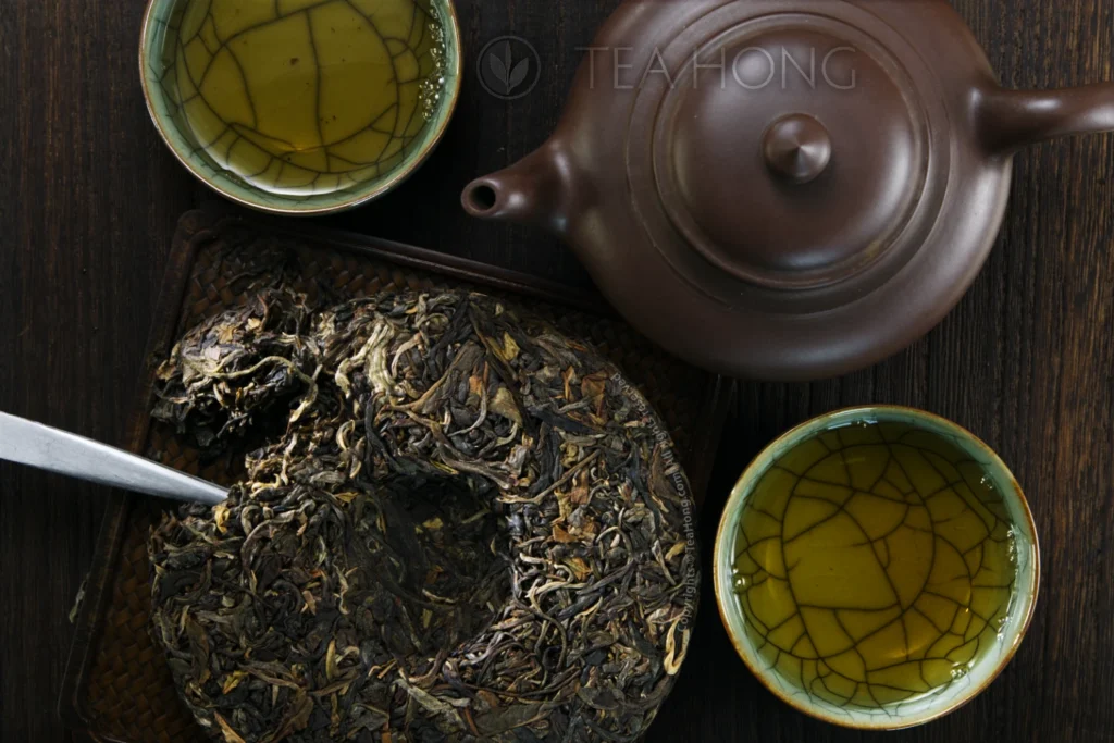 The Inner Primeval Earth cha bing chipped, posed together with a Yixing teapot and two teacups filled with tea