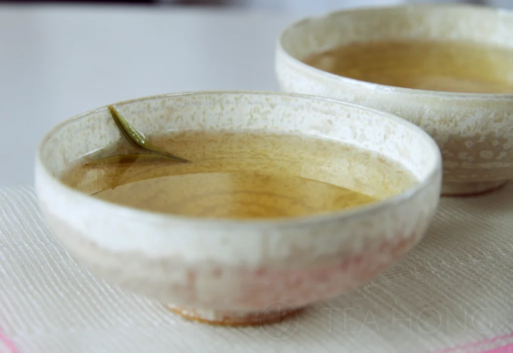 Clear and bright greenish yellow tea liquor in two low profile wide mouth tea cups with very thin bream and light colour body with subtle, and spots of pinkish ash kiln effects