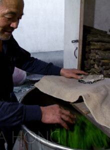 Master Wang feels the softness of the leaves to determine when the process of Sha Qing — arresting enzyme oxidation, in the Western concept of green tea processing — is properly done in his small charcoal fire roaster. Sha Qing — Killing of the Greens