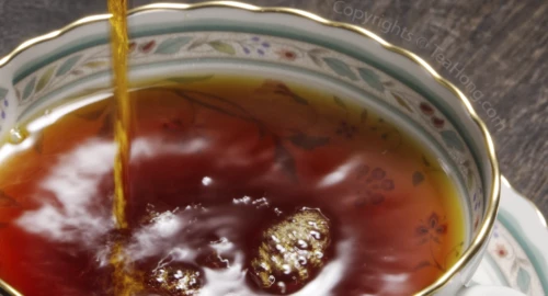 An intensely deep red, transparent tea liquor being poured into a fine porcelain Western style teacup