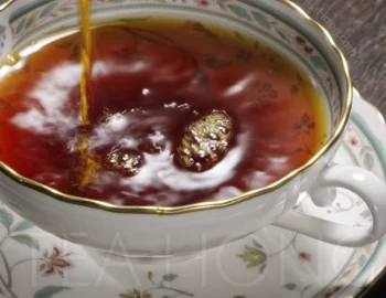 An intensely deep red, transparent tea liquor being poured into a fine porcelain Western style teacup