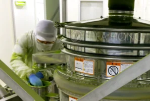 Matcha grinding technician, in full protective overall, head-cover and mask, changing the sieve filter during a halt in the production
