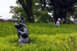 Two human size metal statues in one of the grassland areas, with two visitors walking by Two human size metal statues in one of the grassland areas, with two visitors walking by
